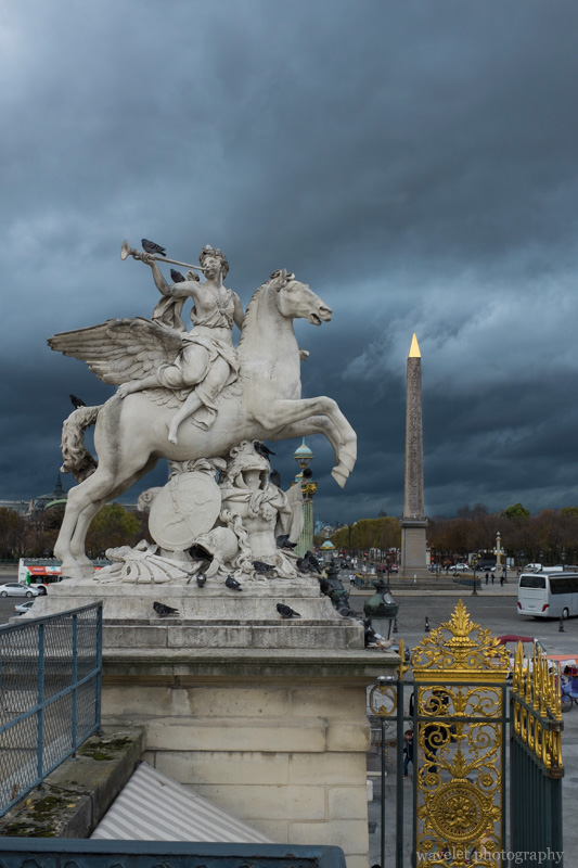 The statue of Renommée riding Pegasus at the west entrance of the Tuileries Garden and the Luxor Obelisk at the Place de la Concorde, Paris